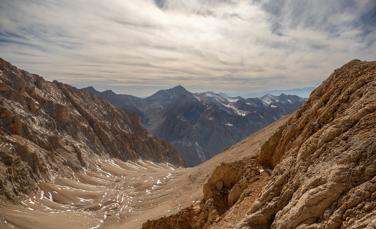 Persona con mal di testa in montagna, circondata da paesaggio montano e segnale di avviso per mal d'altura.